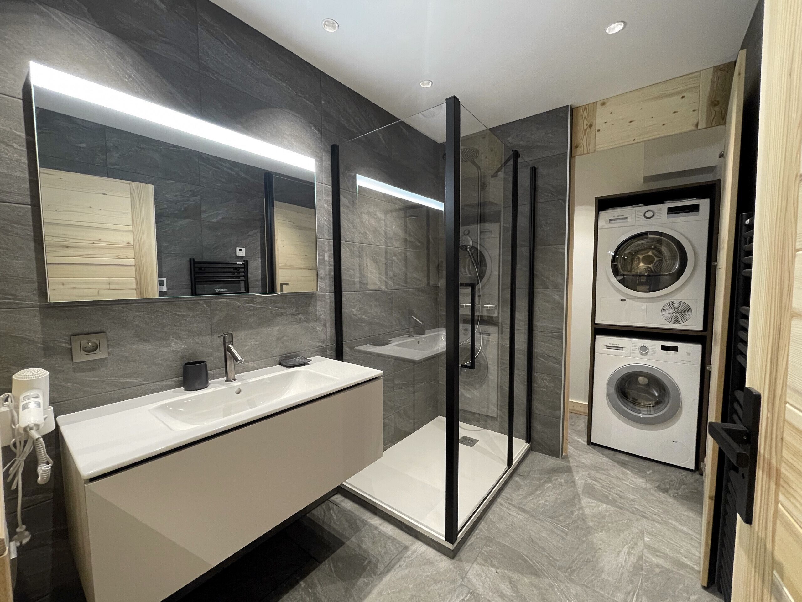 A modern bathroom with a glass-enclosed shower, a white vanity, and a built-in washing machine.