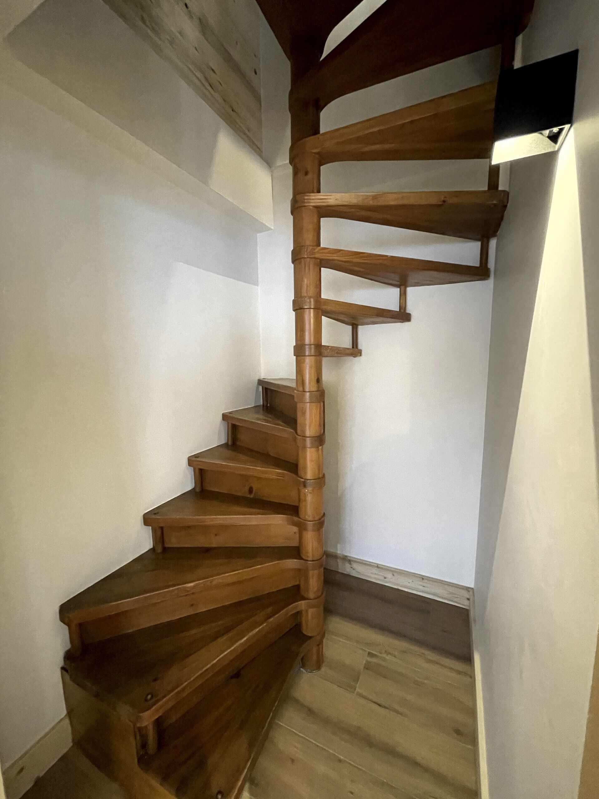 Un escalier en colimaçon en bois, doté d’une rampe, qui mène à l’étage supérieur.