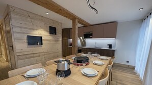 Un'area pranzo moderna con un tavolo di legno apparecchiato per un pasto, una cucina sullo sfondo e un parete in legno con un lampadario.