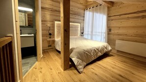 Camera da letto in una baita di legno, con un letto, un comodino, uno specchio e una finestra con tende.