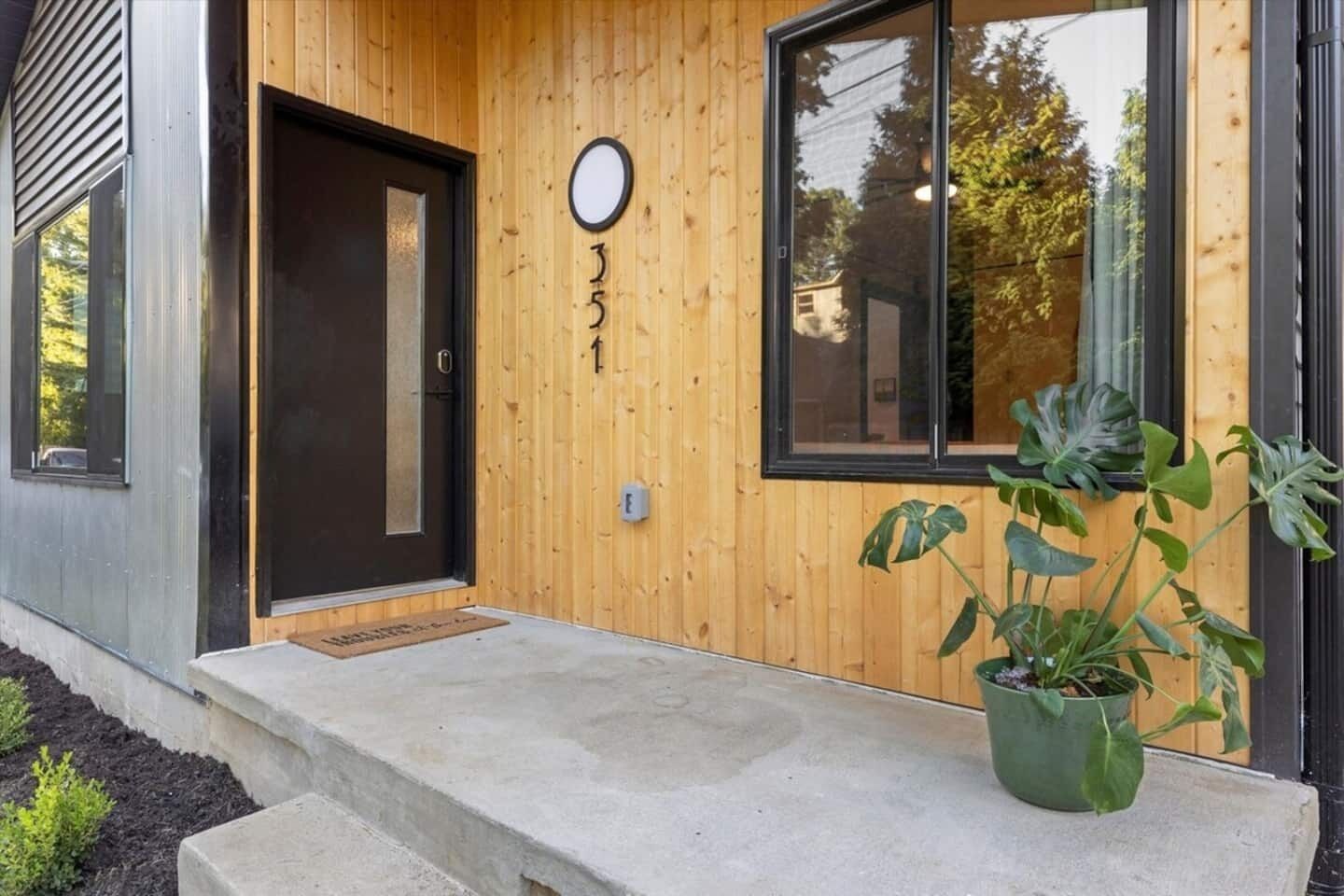 A modern building with a wooden facade, a black door, and a potted plant on the porch.