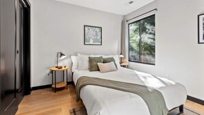 A bedroom with a large bed, two bedside tables, a window with a view of trees, and a door. - Mid-Century 3 BR In Heart of Downtown Lex (Lexington)