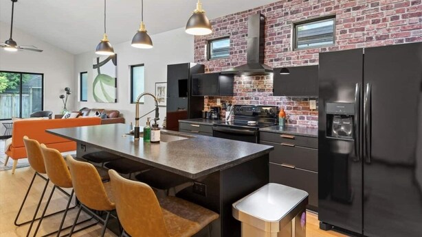 A modern kitchen with a brick wall, black appliances, and a central island with seating. - Mid-Century 3 BR In Heart of Downtown Lex (Lexington)