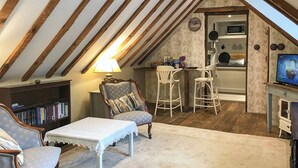 An attic room with a high ceiling, exposed wooden beams, a small kitchen area with a microwave, and a television. - 1 bedroom accommodation in Fernhurst (Fernhurst)