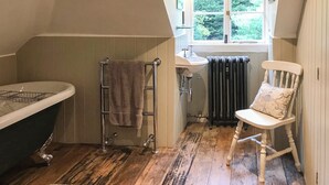 A bathroom with a bathtub, a sink, a radiator, a towel rack, and a chair. - 1 bedroom accommodation in Fernhurst (Fernhurst)