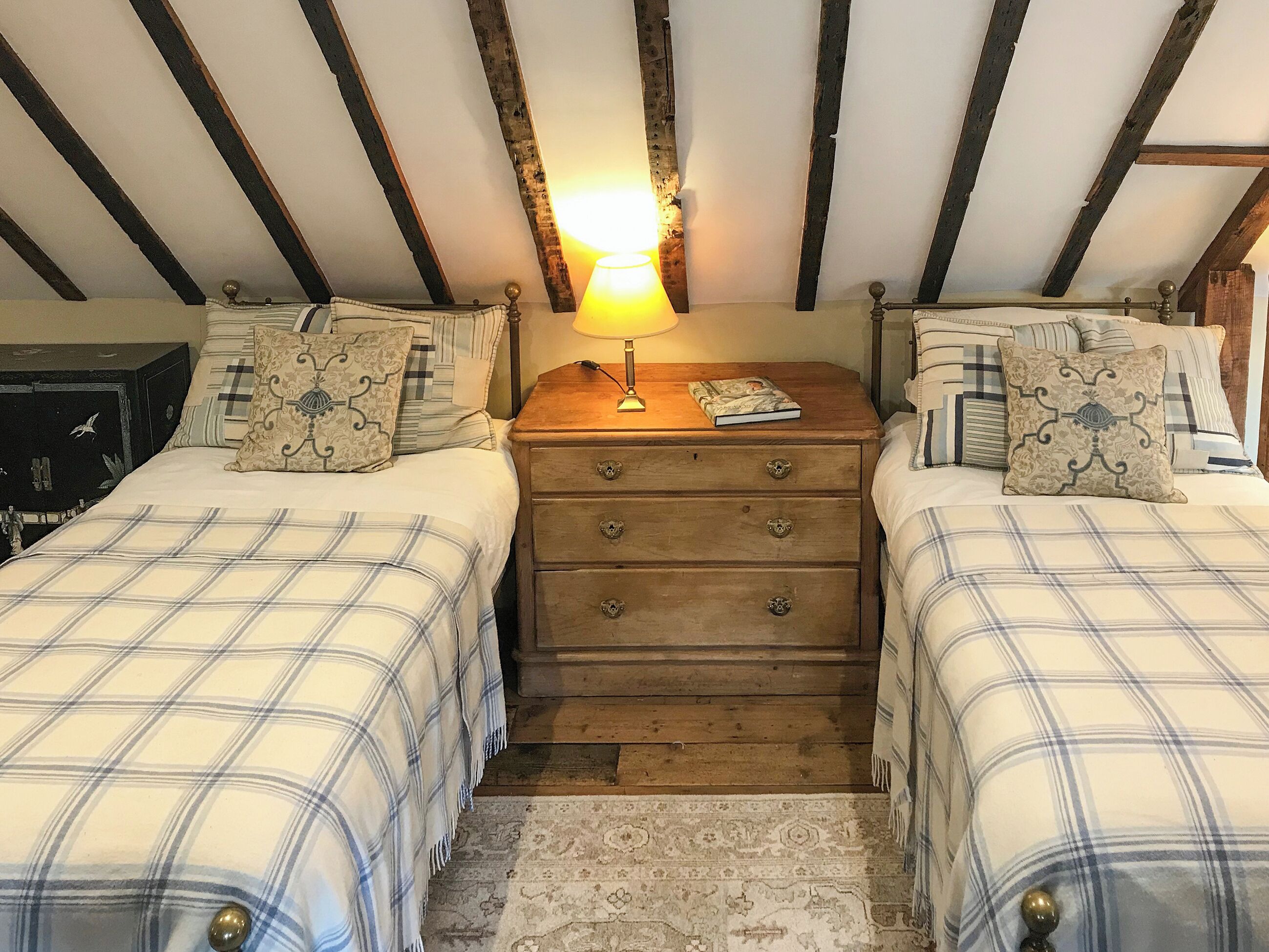 A room with two beds, a wooden dresser, a lamp, and a patterned rug.