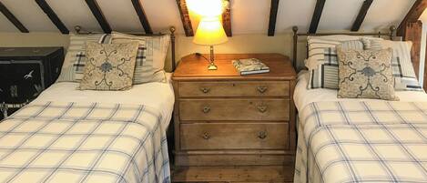 A room with two beds, a wooden dresser, a lamp, and a patterned rug.