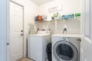 A laundry room with two washing machines, a drying rack, and a trash bin.