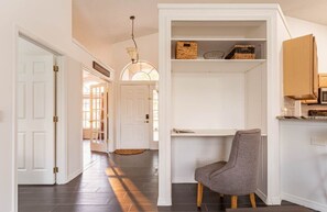 Un pasillo con una silla, un estante con cestas y una puerta que da a otra habitación.