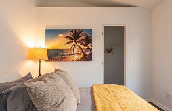 Un dormitorio con cama, lámpara, un cuadro con escena de playa y una puerta.