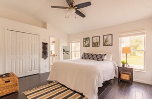 Un dormitorio con una cama grande, un ventilador de techo, una ventana con vistas y una puerta que conduce a otra habitación.