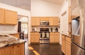 Una cocina con gabinetes de madera, encimera de granito, electrodomésticos de acero inoxidable y salpicadero de azulejos.
