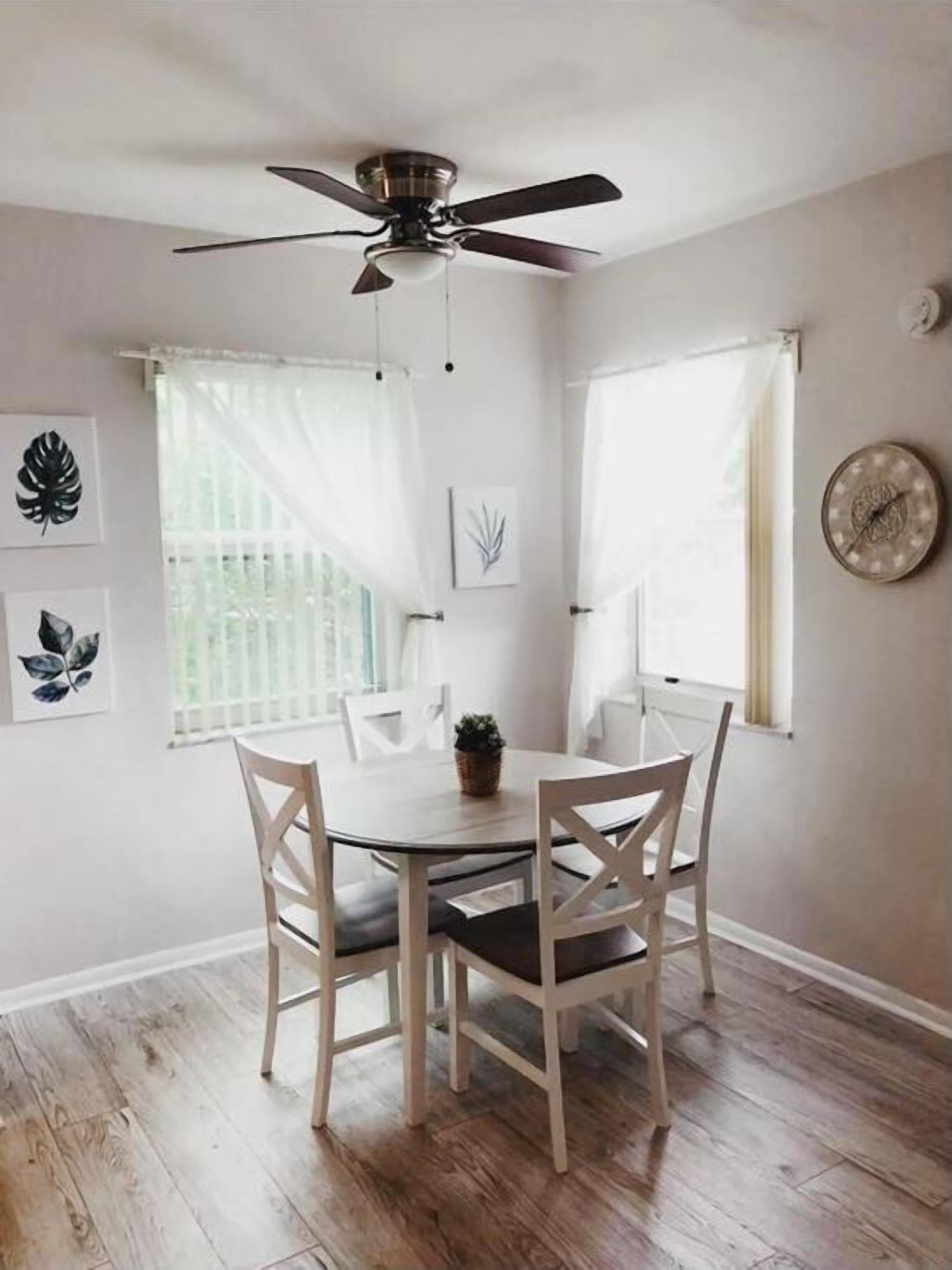 A dining area with a round table and four chairs, a ceiling fan, and a clock on the wall.