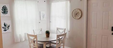 Zona pranzo con un tavolo rotondo, quattro sedie, una ventola a soffitto e una porta con un orologio appeso al muro.