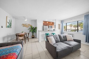 A modern living room with a grey sofa, a colorful bed, a dining area with wooden chairs, and a kitchen with wooden cabinets and a microwave. - Bayview Apartments by Lowkl (Fort Lauderdale)