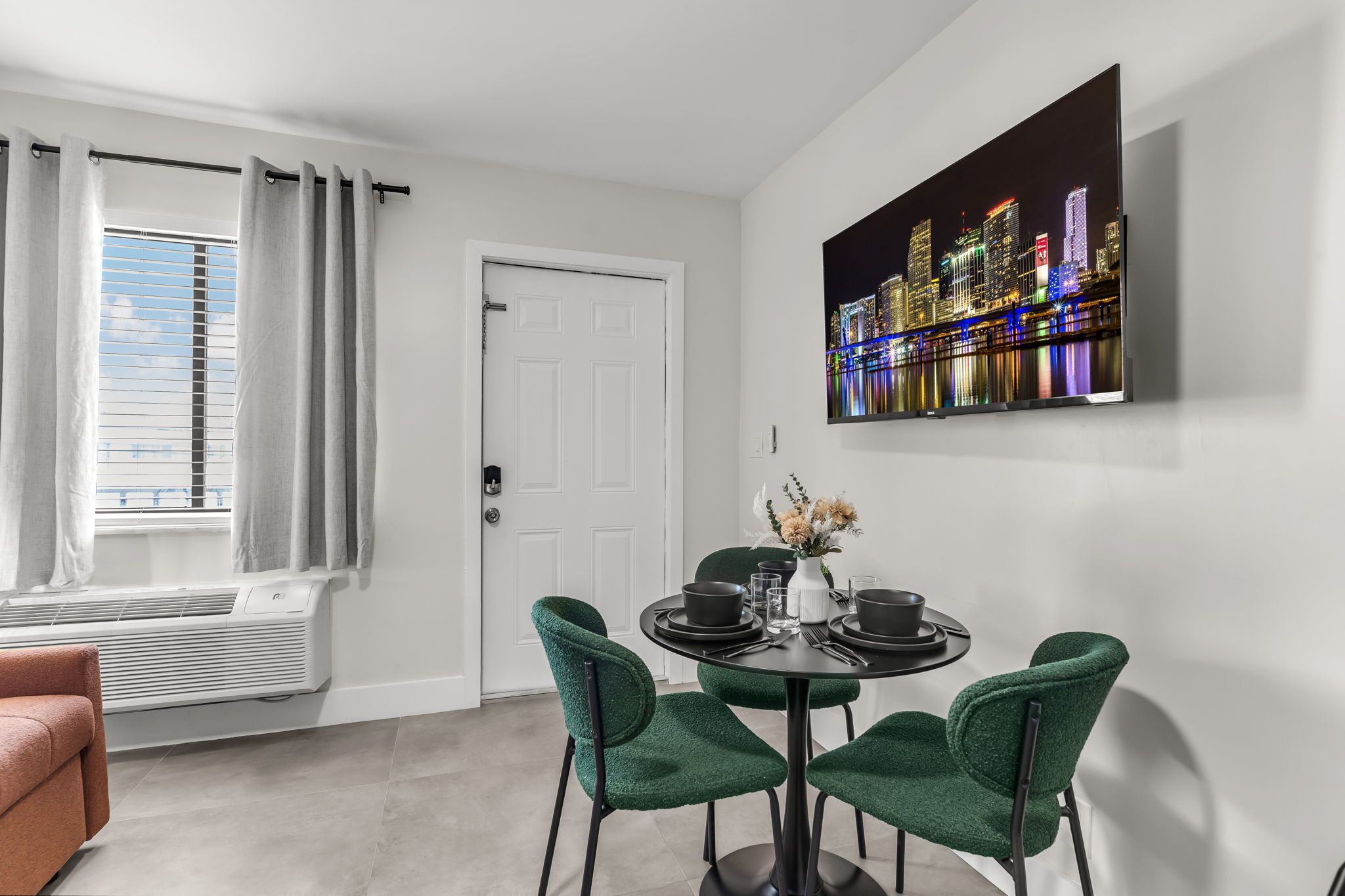 Une pièce moderne avec une table à manger, des chaises vertes, une porte blanche et un tableau représentant un paysage urbain.