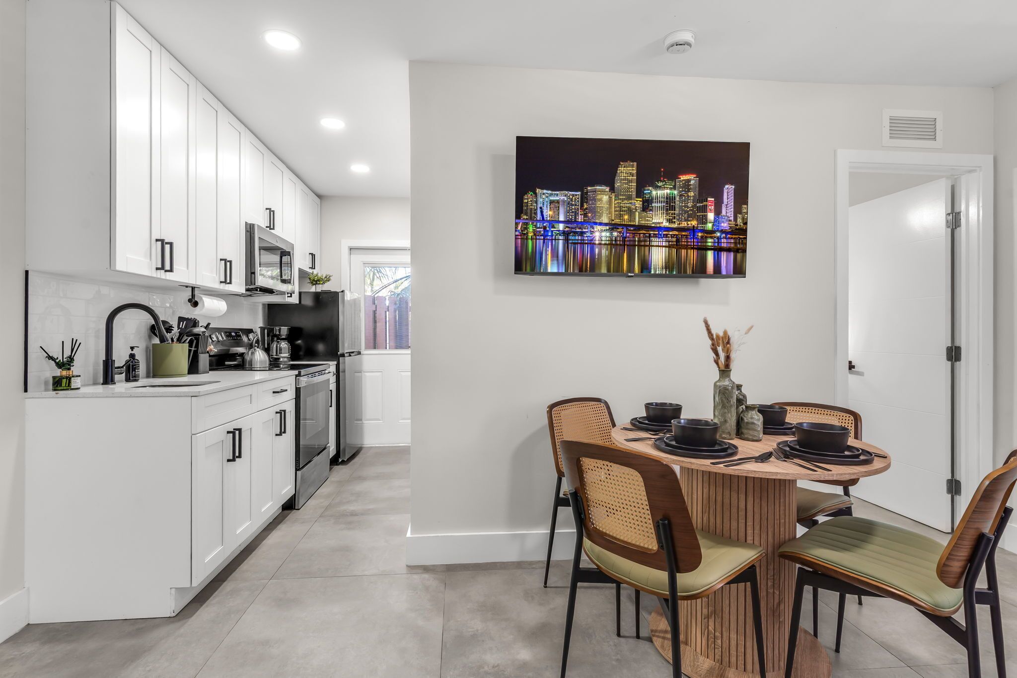 Une cuisine moderne avec des meubles blancs, un coin repas doté d’une table ronde et un tableau représentant un paysage urbain accroché au mur.