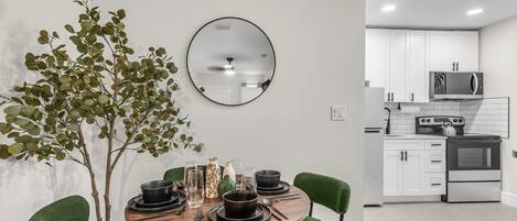 Un'area pranzo moderna con un tavolo rotondo, sedie verdi, una pianta in vaso e una cucina sullo sfondo.