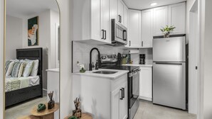 A modern kitchen with white cabinetry, a stainless steel refrigerator, and a microwave. - Bayview Apartments by Lowkl (Fort Lauderdale)