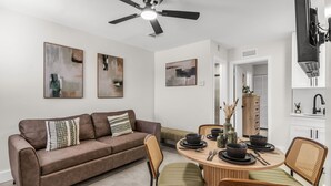 A modern living room with a brown sofa, a dining table set with black bowls and plates, and a ceiling fan. - Bayview Apartments by Lowkl (Fort Lauderdale)