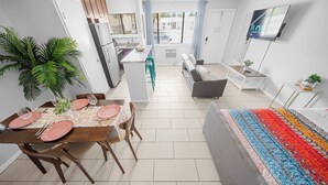 A modern living room with a sofa, a dining table set with pink plates, and a colorful rug. - Bayview Apartments by Lowkl (Fort Lauderdale)