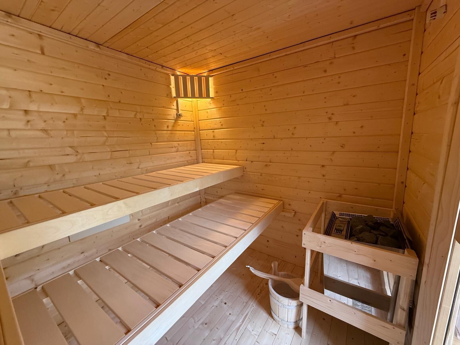 A wooden cabin with bunk beds, a small table, and a bucket.