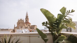 A view of a historic church with a tall bell tower, surrounded by modern buildings and greenery. - Suite1212 Rattazzi (Monopoli)