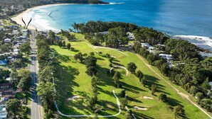 An aerial view of a coastal area with a golf course, beachfront properties, and a road leading to the beach. - Mariners 3 - The closet apartment to Mollymook Beach, you can almost touch it! (Mollymook)