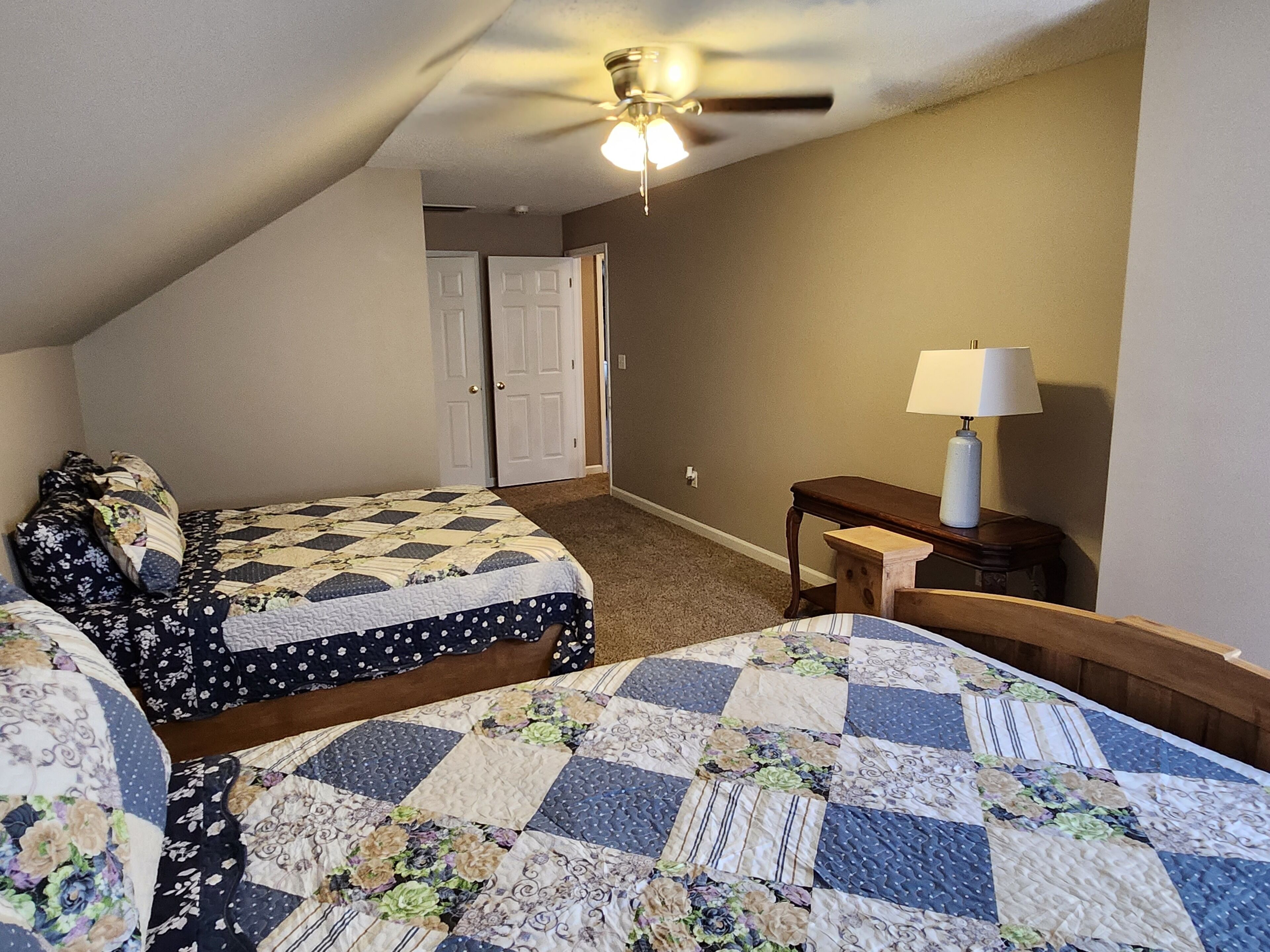 A bedroom with two beds, a ceiling fan, a nightstand, and a lamp.