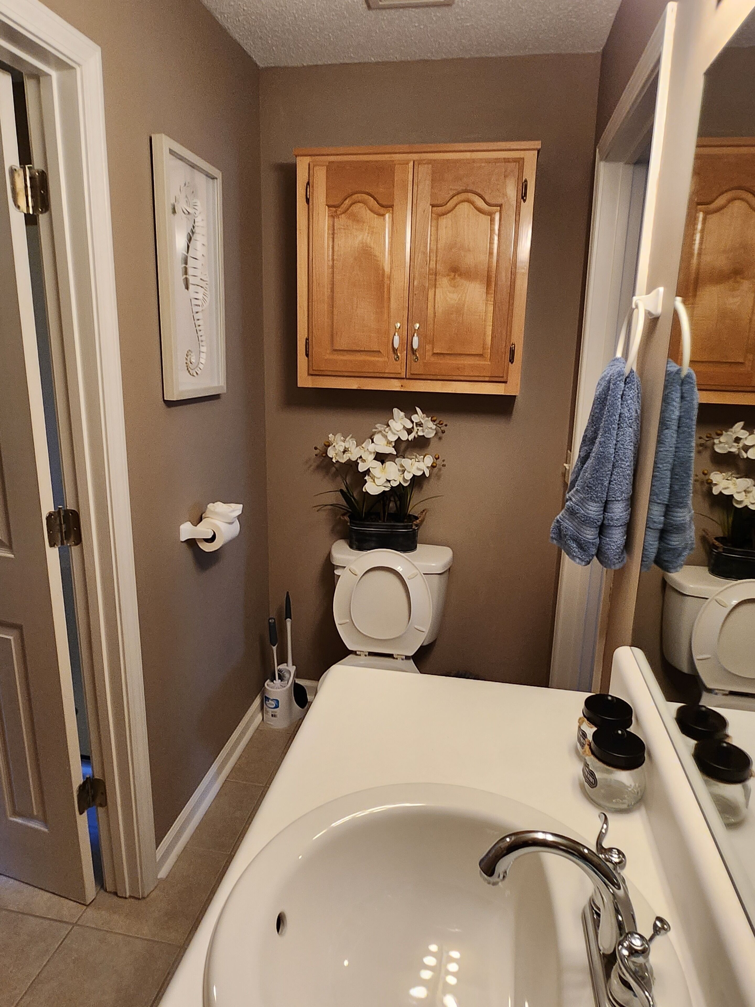 Une salle de bain avec un lavabo blanc, des meubles en bois, des toilettes et un miroir.