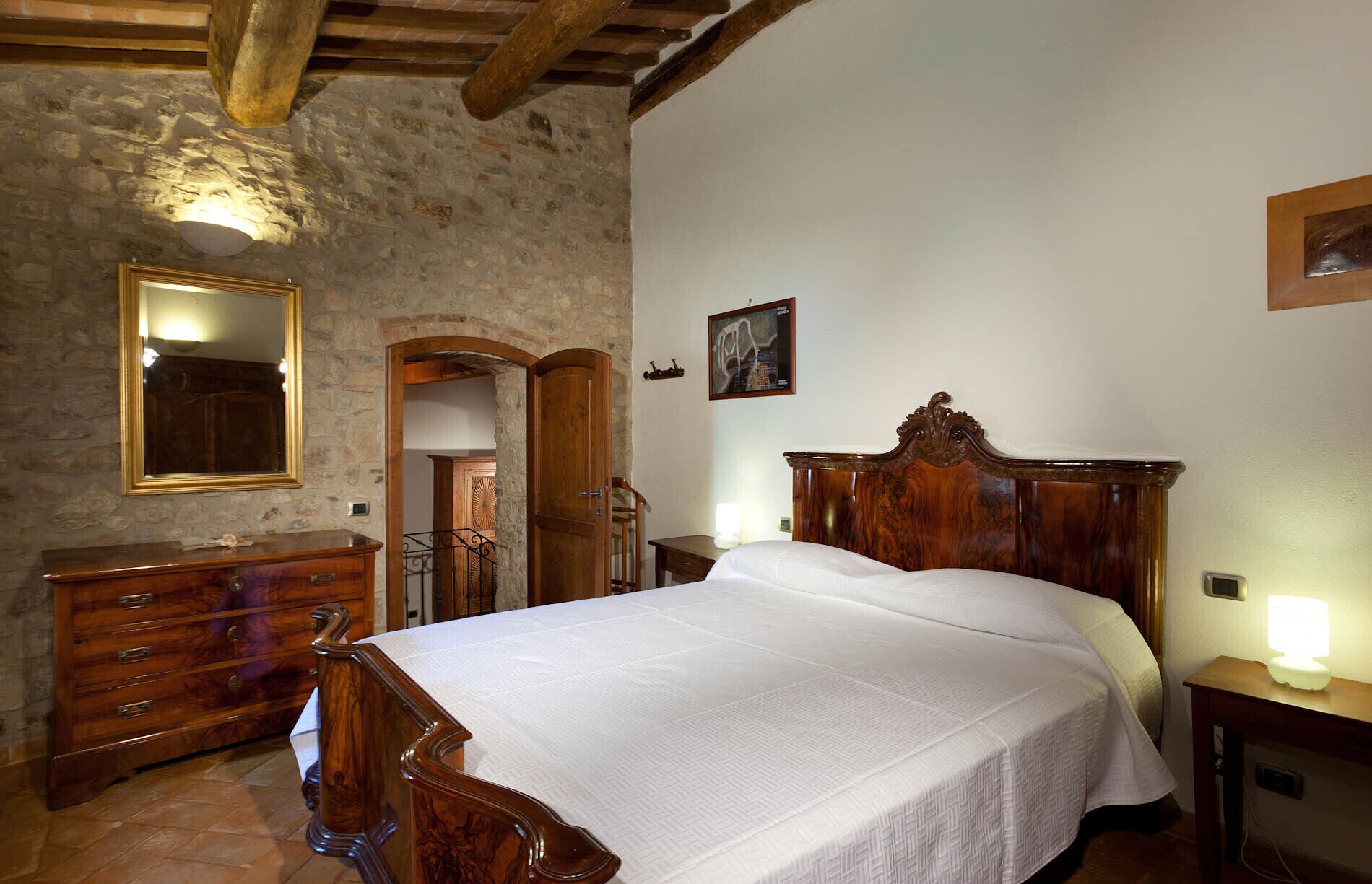 A bedroom with a wooden bed, a dresser, a mirror, and a stone wall.