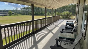 A covered outdoor area with a wooden deck, benches, and a view of a grassy field. - Farm to Beach in 15 Minutes (Panama City Beach)