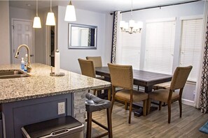 A modern kitchen with granite countertops, a built-in island, and a dining area with wooden chairs and a dark wood table.