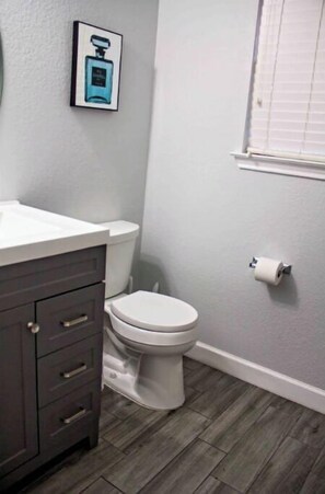 A bathroom with a white toilet, a dark wooden vanity, and a framed picture on the wall.