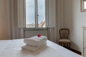 Habitación de hotel con cama, una silla y ventana con vista a edificios.
