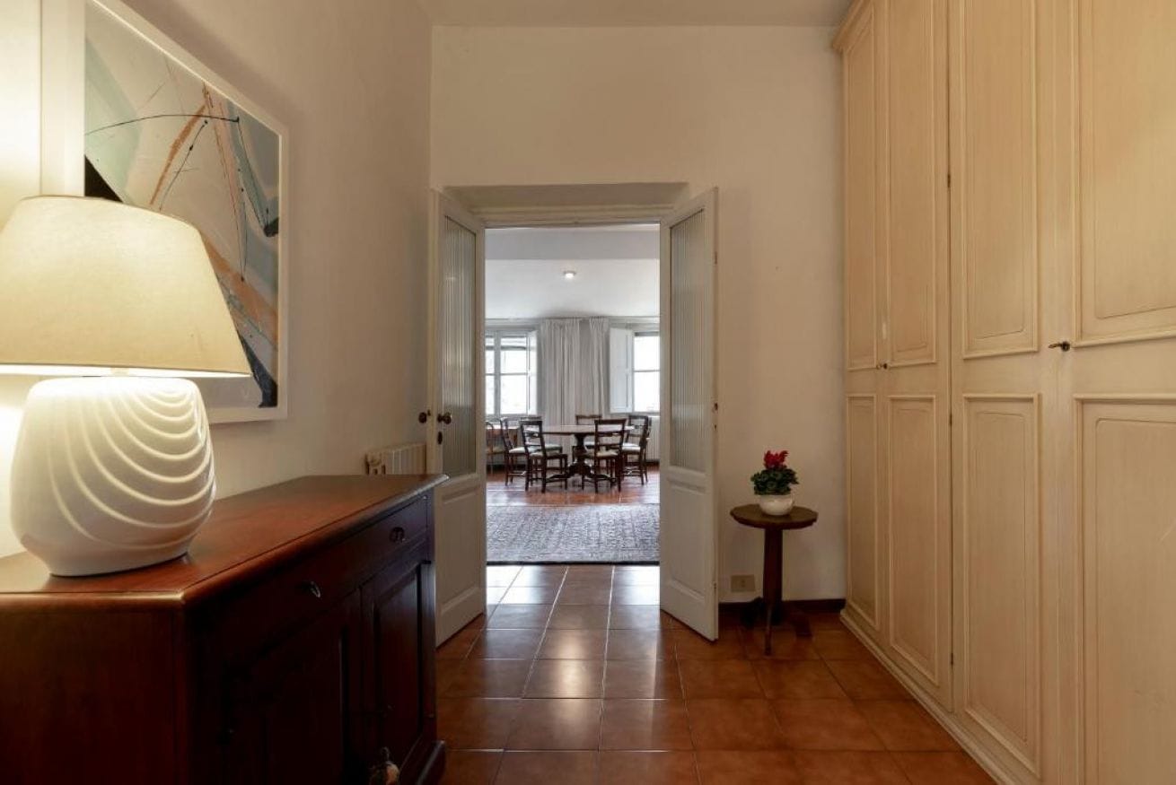 A hallway with a lamp, a painting, and a view into a dining area.