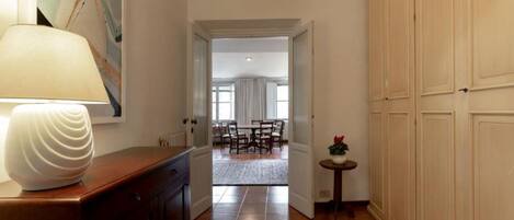 A hallway with a lamp, a painting, and a view into a dining area.
