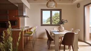 Una cocina moderna con armarios de madera, una zona de comedor con mesa y sillas blancas, y un ventanal con vistas a zonas verdes.