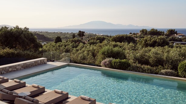 Zona de piscina con sillas de descanso y vistas al mar y a las montañas.