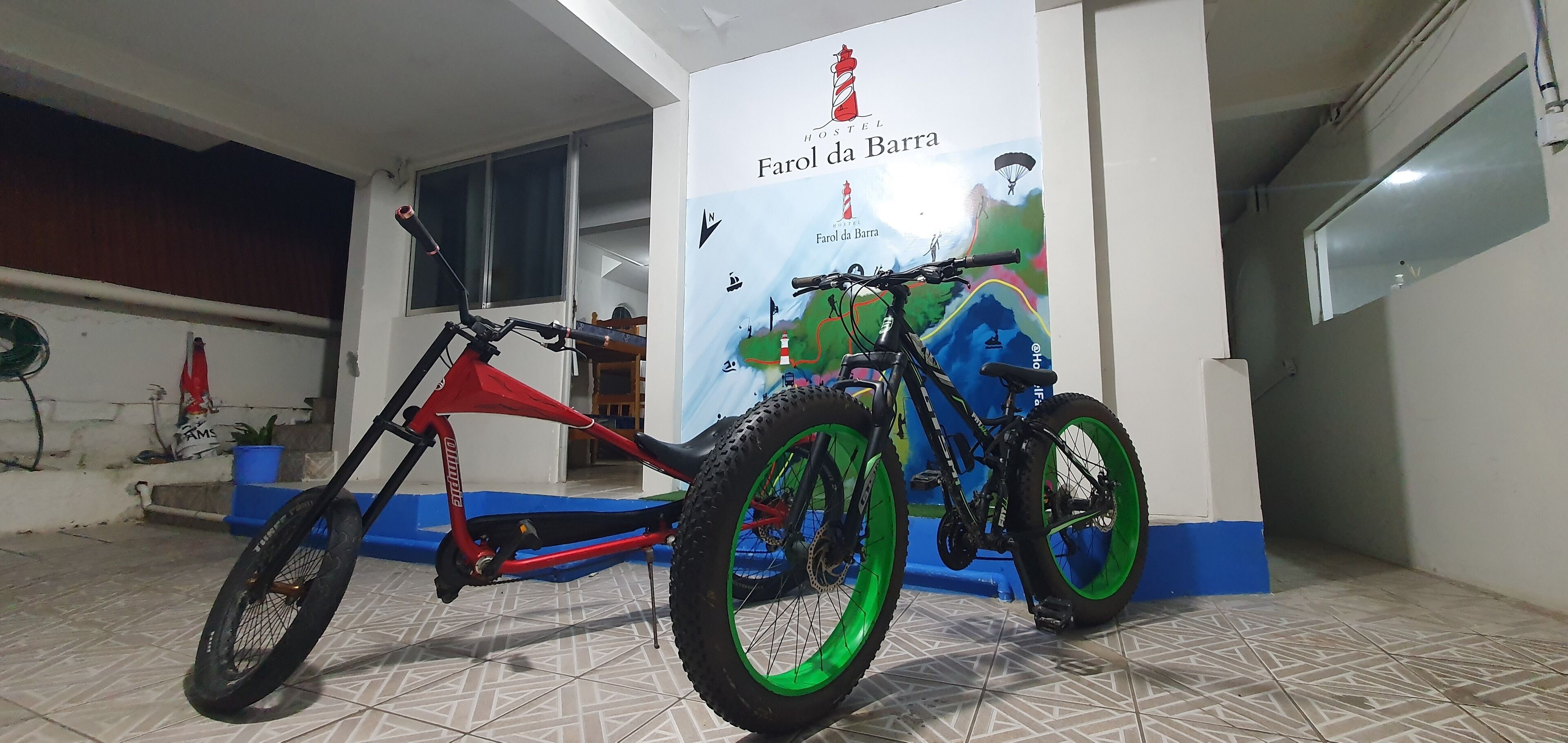 A bicycle in a room with a poster of a lighthouse and a mountain.