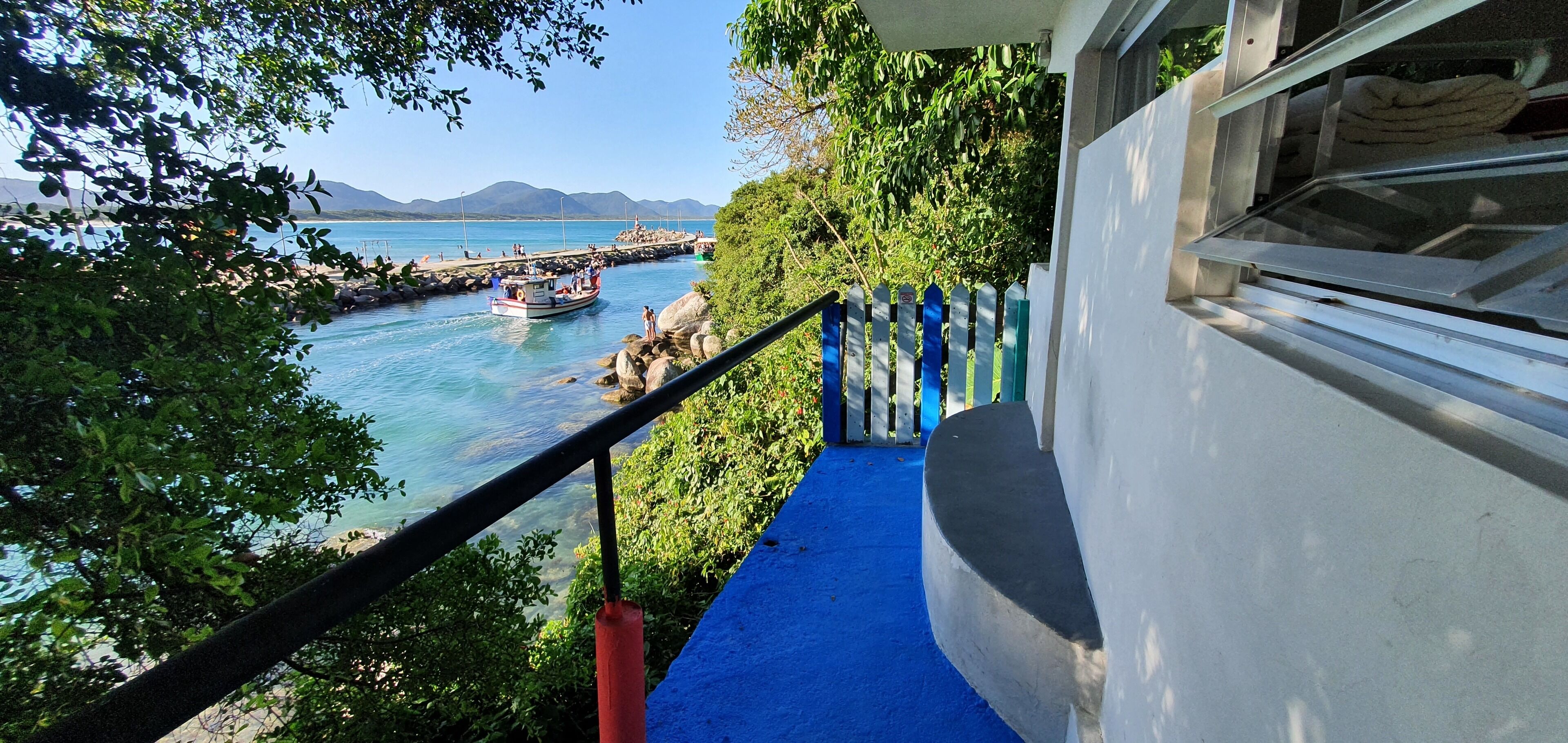 Blick auf die Küste mit einem Boot an einem Steg, einer Treppe, die zu einem Gebäude führt, und einem wolkenlosen, blauen Himmel.