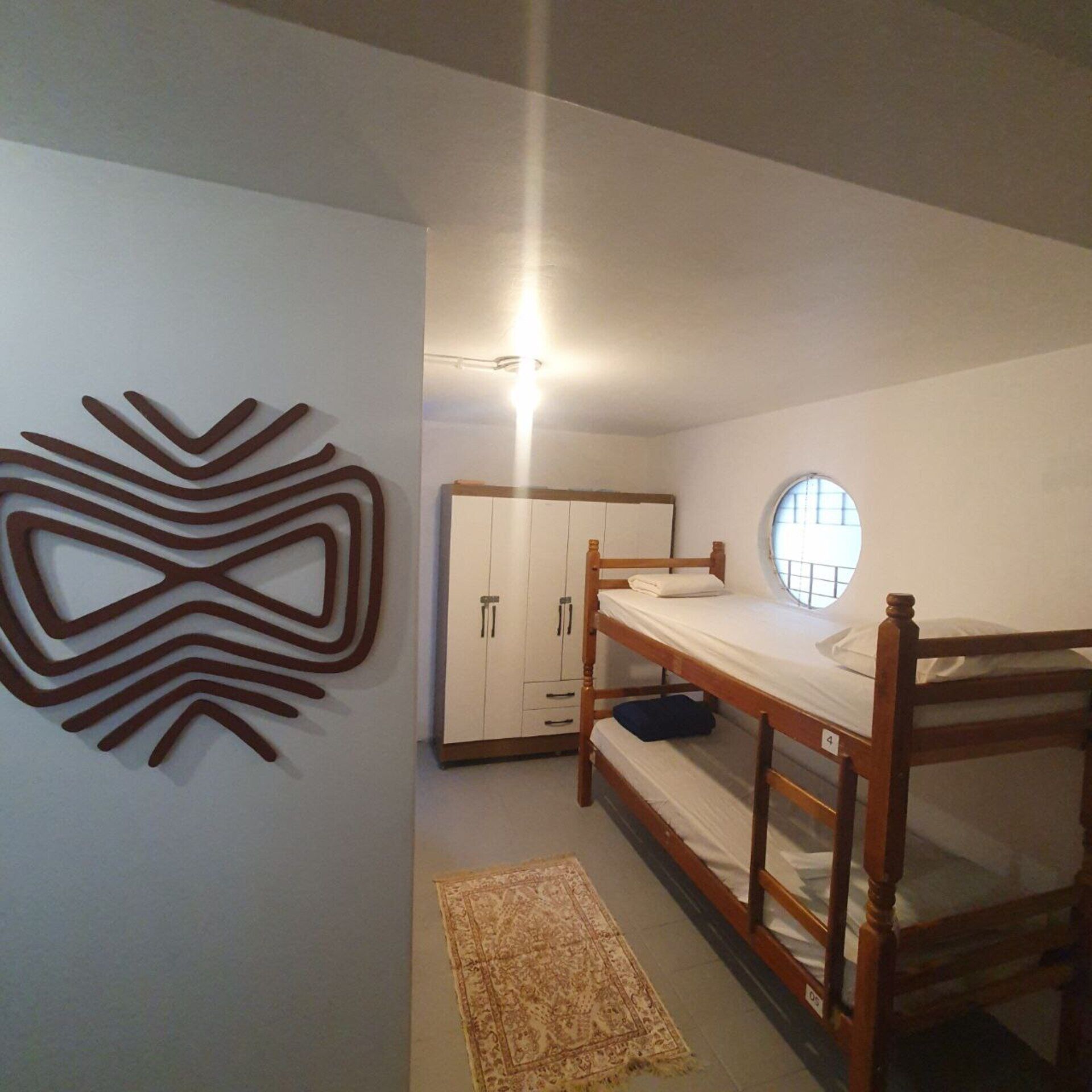 A bedroom with a bunk bed, a wardrobe, a decorative wall piece, and a small rug.