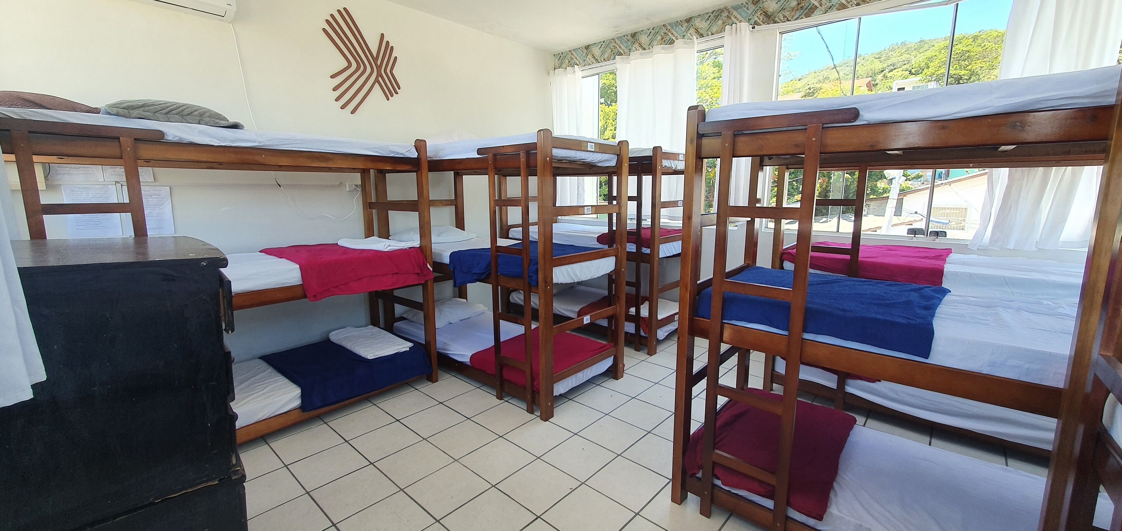 A dormitory room with bunk beds, tiled floor, and a window with a view of greenery.
