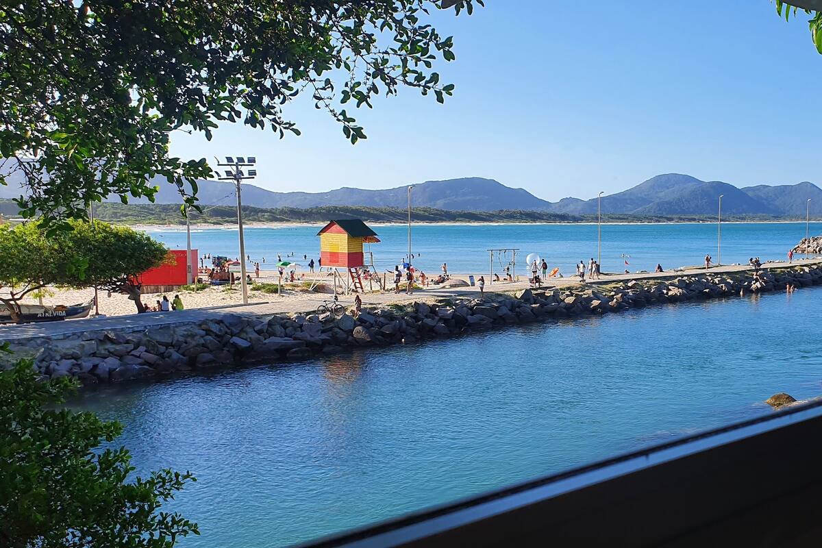 Une plage avec une tour de surveillance pour les sauveteurs, un rivage rocheux et des montagnes en arrière-plan.