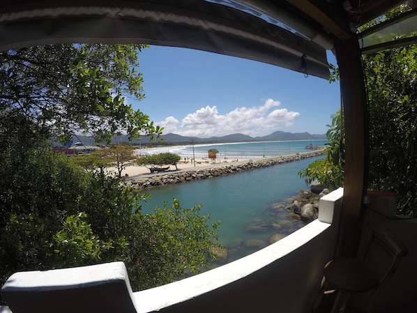 Vista desde un balcón sobre una playa con cielo despejado, costa rocosa y una cadena montañosa distante.