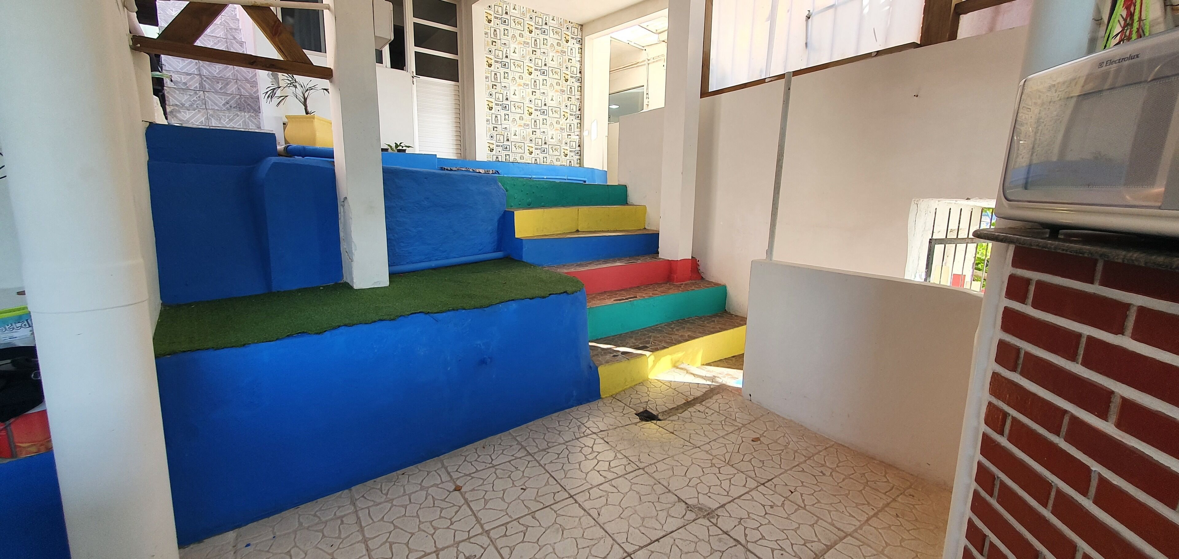 A compact kitchen with a microwave, a tiled floor, and a staircase with colorful steps.