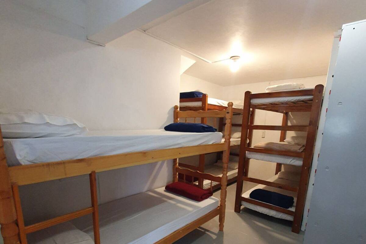 Une chambre de dortoir avec des lits superposés, une porte blanche et un luminaire au plafond.