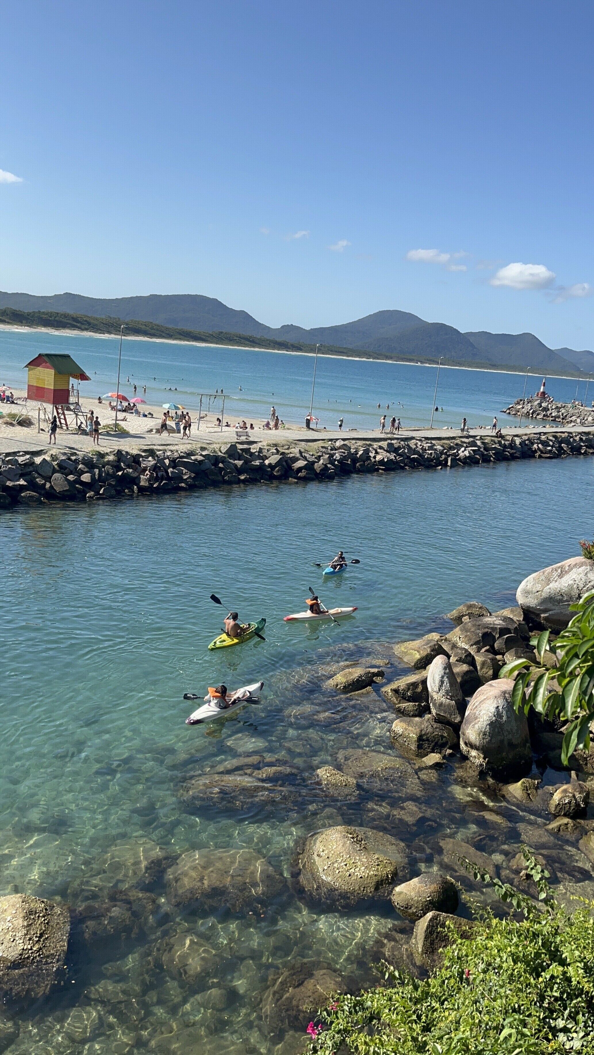 Una playa con kayakistas, una torre de salvavidas y costas rocosas.