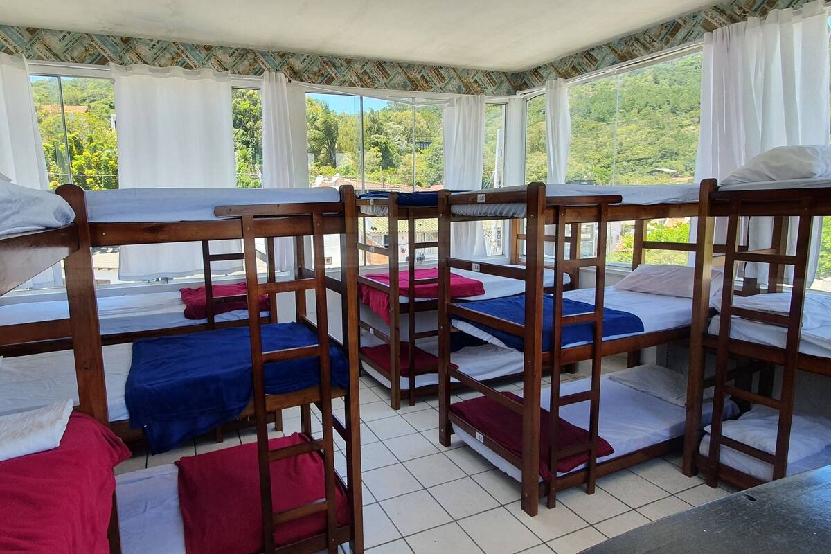 Une chambre de type dortoir, avec des lits superposés, de grandes fenêtres et une vue sur la verdure environnante.