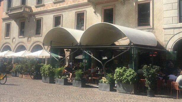 An outdoor café with a covered seating area, potted plants, and a cobblestone pavement. - The most glamorous lounge in downtown: romantic sensory and rock! (Bergamo)